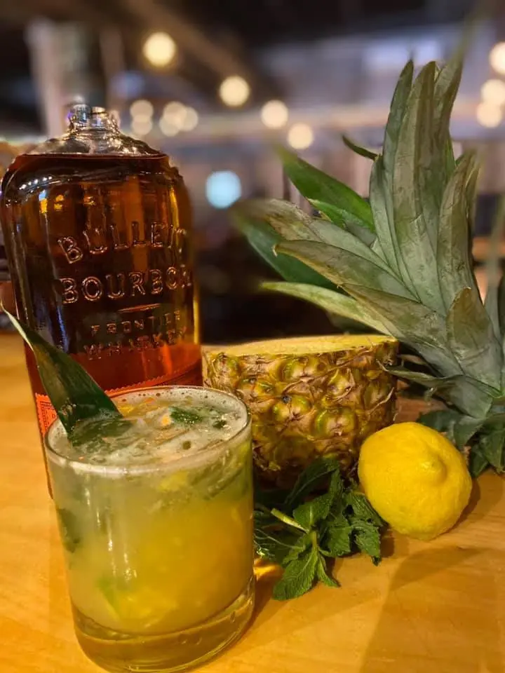 Bourbon cocktail with mint beside a bottle and pineapple