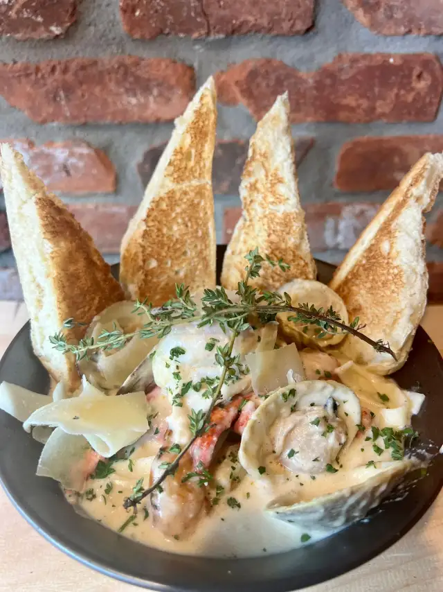 Creamy seafood pasta with toasted bread on a brick-backed table